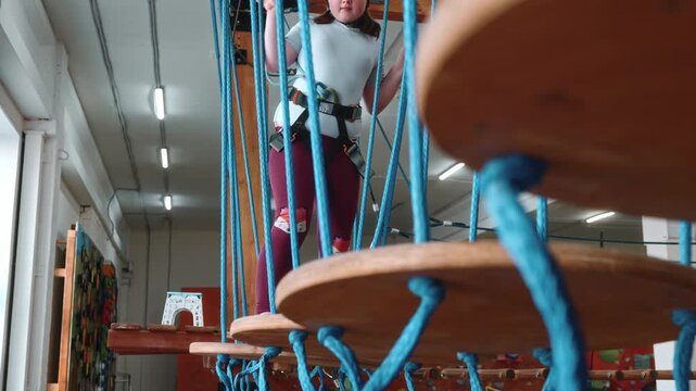 A beautiful cinematic perspective in a rope park with suspended platforms. A brave 10-year-old girl is being tested on staggering platforms. Extreme sports on children's holidays. Healthy lifestyle