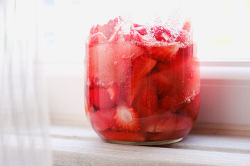 Strawberries waiting in the sun with sugar in a jar on the edge of the window. Homemade liqueur, alcoholic drink