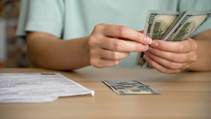 A young woman counts out cash to pay her utility bills. Home finances. Routine concepts.