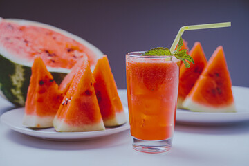 Refreshing watermelon freshly squeezed juice or smoothie with mint and lemon and sliced watermelon in bokeh on a light background. Selected focus