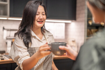 Obraz premium Portrait of asian barista woman small business owner working behind the counter bar and receive order from customer on coffee packaging and cup of coffee background in cafe or coffee shop.