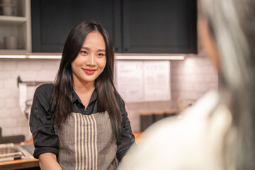 Portrait of asian barista woman small business owner working behind the counter bar and receive order from customer on coffee packaging and cup of coffee background in cafe or coffee shop.