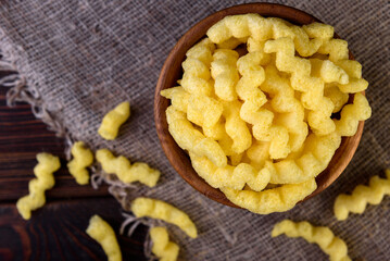 Cheese corn sticks in wooden bowl on dark wooden background.