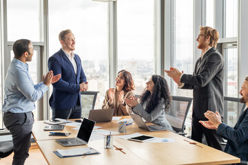 A business team is gathered around a conference table in a modern office with large windows. They...