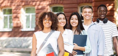 Student Cohort. Group of smiling multicultural teens posing near university campus, holding workbooks and looking at camera