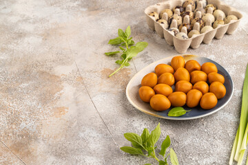Pile of smoked quail eggs on plate on a brown concrete background. side view, copy space.