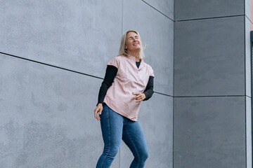 Happy positive dancer curling in dance. Woman with blond hair dancing on urban street, on gray wall...
