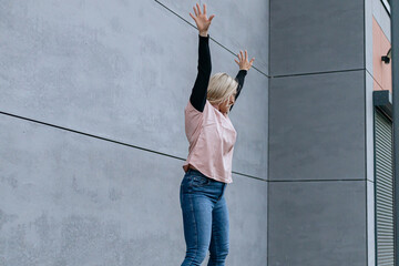 Happy positive dancer curling in dance. Woman with blond hair dancing on urban street, on gray wall...
