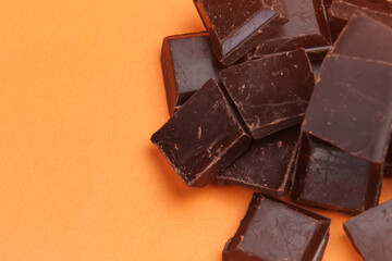 Pure organic dark bitter chocolate pieces on a creative orange color background