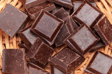 Delicious dark broken chocolate parts in eco friendly rustic rattan bowl close up