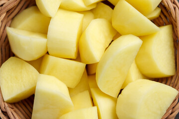 Sliced raw peeled organic potatoes in rattan wicker eco friendly rustic bowl closeup. Uncooked healthy vegetable ingredient.