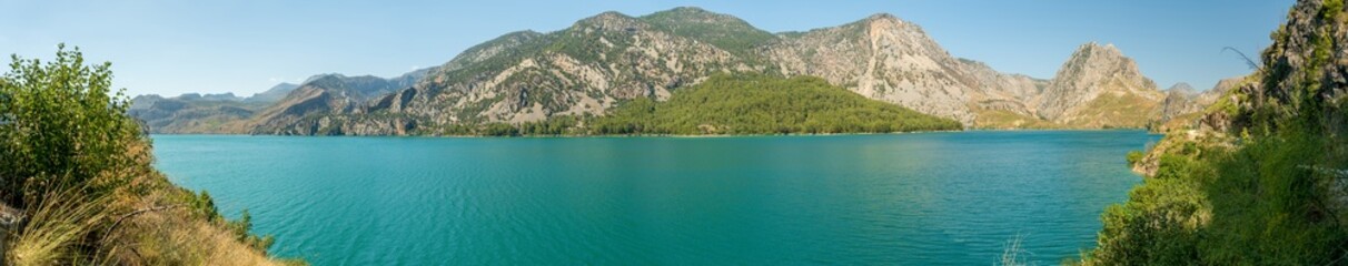A Wide-Angle Panoramic Shot of a Pristine Mountain Lake, Surrounded by Forested Slopes and Rugged Cliffs, the Crystal Clear Water Reflecting the Majestic Landscape.