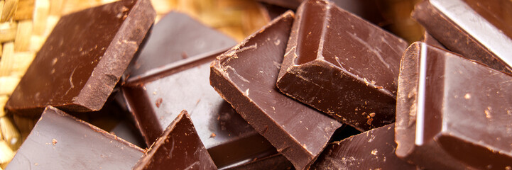 Dark bitter broken chocolate pieces in rustic eco friendly wicker bowl. Web banner design element