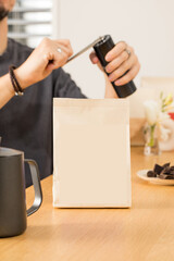 Blank paper bag near man barista grinding coffee beans