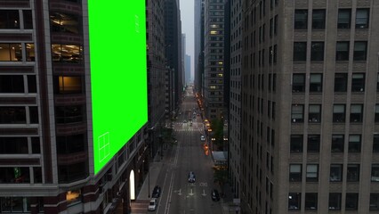 Urban street in USA city with a green screen billboard on a skyscraper with tracking markers. Aerial of downtown American cityscape at dusk