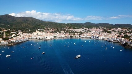 Naklejka premium aerial view over the Badia de Cadaqués, to the old white houses of Cadaqués, Port Alguer and the turquoise water of the Mediterranean Sea, mountains of the Pyrenees behind, Girona, Catalonia, Spain