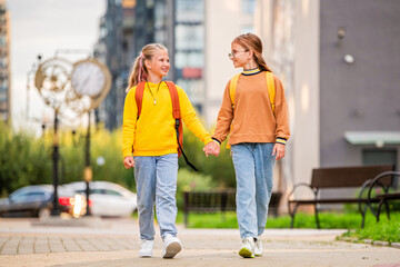 Two happy children walk to school with backpacks along a sunny city street.