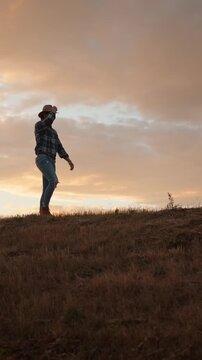 A Cowboy, Silhouetted, is Walking on a Grassy Hill at Sunset under the Western Skyline
