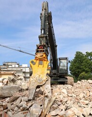 Obraz premium Heavy excavator with shear attachment on a heap of debris during a building demolishment for a redevelopment.