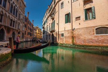 Venice, Italy - June 05, 2024: A gondolier is waiting for tourists on the bridge over the canal. Popular tourist attractions in Venice. Long exposure shot.