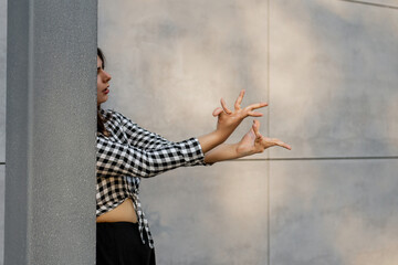 Happy positive dancer curling in dance. Woman with long dark dancing on urban street, on gray wall...