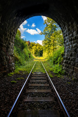 Tunnel on railway line between Menden and Balve Germany in green natural landscape of Sauerland. Symmetric perspective from darkness into bright sunlight. Sunny summer forest near Klusenstein castle.