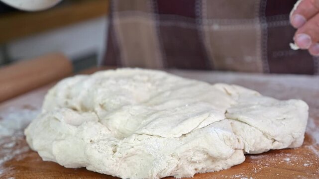 In a home kitchen, a man kneads pizza dough on a wooden board. Preparing a family meal with natural light highlighting the real kitchen setting.