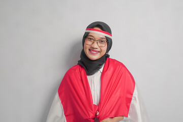 A young woman wearing a hijab and glasses, smiling while holding a red and white scarf.