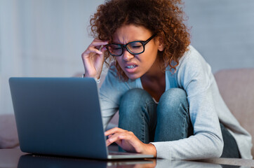 Afro woman with eyesight problem using laptop, trying to read online content