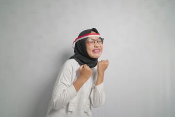 A woman wearing a hijab and glasses with a red and white headband celebrating