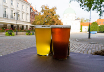 Two glasses of beer, light and dark cold drink on a old European city blurred background, historic buildings