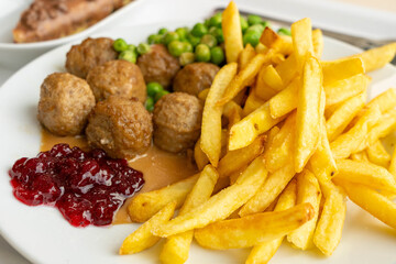 Meatballs with french fries, green peas, bechamel sauce and cranberry jam, meat balls on white plate