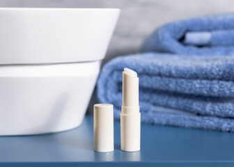 Opened lip balm stick on blue conutertop near cosmetics and basin in bathroom, mockup