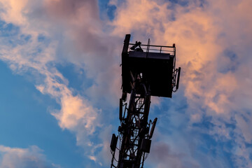 Signal tower or cell phone tower against the sky with white clouds 