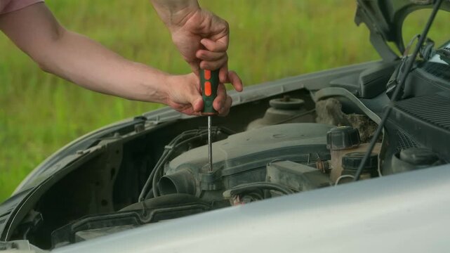 Man tightens screws to secure engine components in place. Guy pauses to check alignment of screws. Male lowers hood signalling end of work on engine
