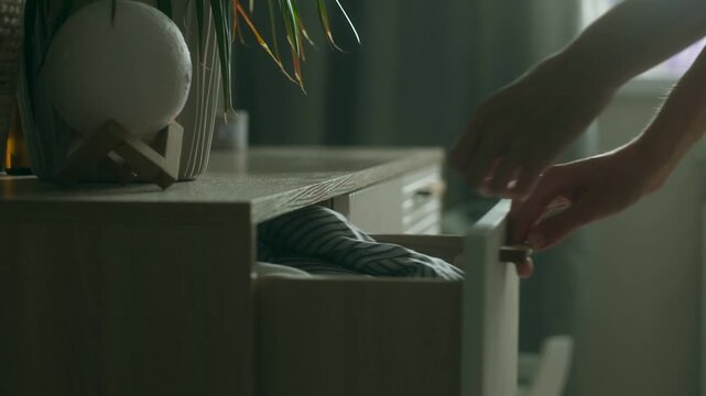 Woman opens door of cabinet and places neatly folded blouse into dresser drawer. Female puts thing neatly on shelf to maintain tidy appearance in bathroom