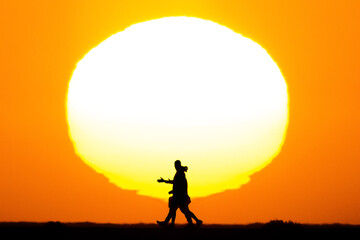 Silhouette of people walking at sunset with a huge sun in the background