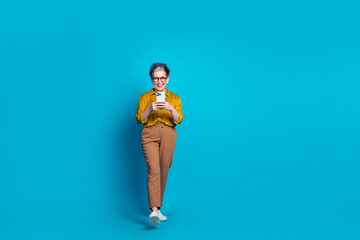 Full length photo of adorable good mood lady dressed shirt eyewear typing modern gadget empty space isolated blue color background