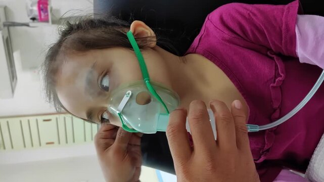 Hand-helping Asian kid using nebulizer masks, breathes in steam, coughs, uses an oxygen spray inhaler, and has a stuffy or runny nose. 4K Vertical