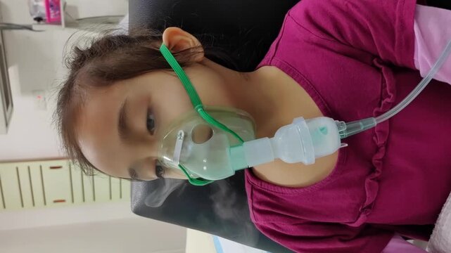 An Asian kid using nebulizer masks by themselves smokes, breathes in steam, coughs, uses an oxygen spray inhaler, and has a stuffy or runny nose. 4K Vertical