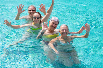 Group of four cheerful friends having fun in outdoor swimming pool under the sun. Vacation and relax concept