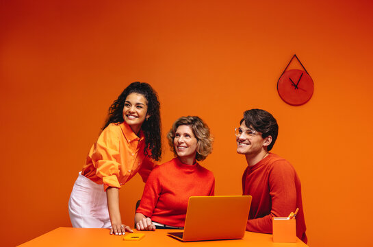 Happy business team in a vibrant monochromatic workspace with orange accents