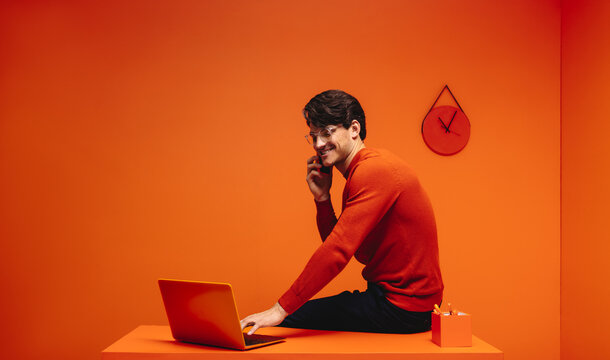 Man working in vibrant monochromatic office, using laptop and phone for creative tasks
