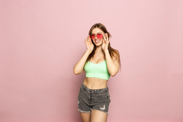 Young Beautiful Woman In Green Top Posing In Sunglasses On Pink Background