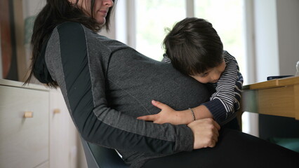 Pregnant woman with her young child embracing her belly, capturing a candid and tender moment of love and connection between mother and child at home