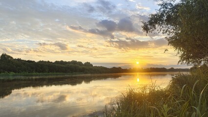 On an early summer morning, the sun rose over the forest on the far side of the river, breaking...