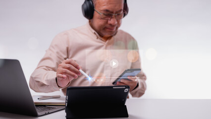 Adult learning, Seniors in technology classes with tablet for streaming video online in classroom. A man is sitting at a desk with a laptop and a tablet. He is wearing headphones