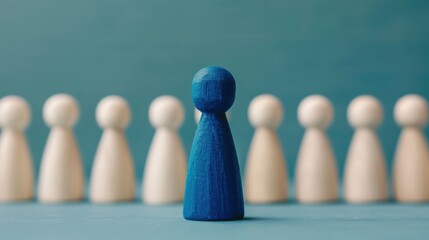 Abstract concept of individuality and leadership with a blue wooden figure standing out among white wooden figures on a teal background.