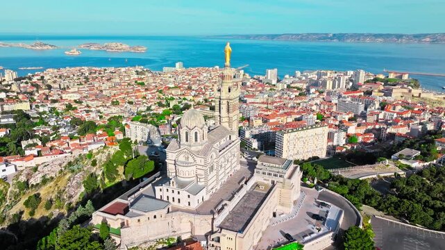 Grand basilica on top of a hill crowned by a golden statue, old city centre and port by blue Mediterranean sea coast in Marseille, France. Basilica of Notre Dame of la Garde at Marseille in France.