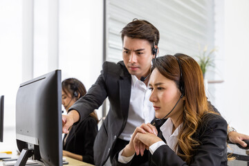 Focused call center agents receiving guidance from supervisor during training session. Asian man...